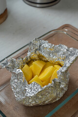 Top view of raw seasoned potatoes in foil ready for baking on a wooden table.