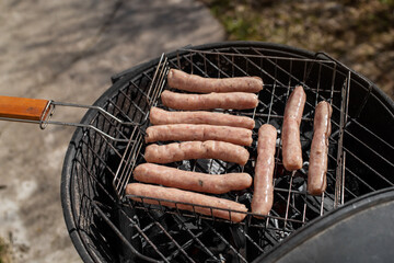 Top view of raw chicken sausages on the grill. Grilling sausages outside on a barbecue grill. First outdoor grill party in the spring season. Sunny spring day.