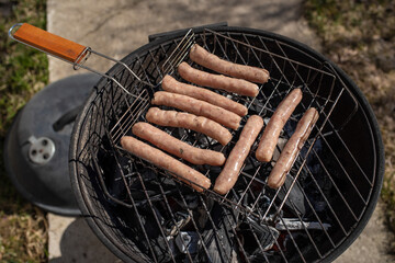 Top view of raw chicken sausages on the grill. Grilling sausages outside on a barbecue grill. First outdoor grill party in the spring season. Sunny spring day.