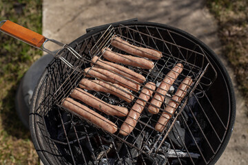 Top view of raw chicken sausages on the grill. Grilling sausages outside on a barbecue grill. First outdoor grill party in the spring season. Sunny spring day.