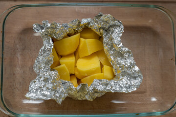Top view of raw seasoned potatoes in foil ready for baking on a wooden table.