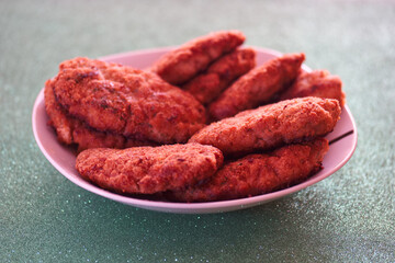 Crispy fried chicken pieces served on a white plate against a vibrant green background during a casual gathering