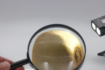 Magnifying glass held over golden powder with bright lights illuminating the subject in a close up...