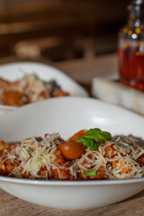 Healthy homemade Mediterranean dish - fusilli pasta with tomato sauce in a white bowl with cheese on top on the wooden table. Pasta bolognese.