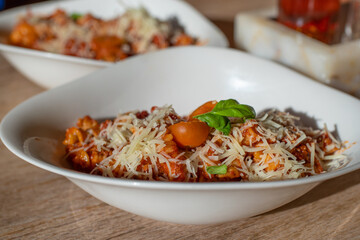 Healthy homemade Mediterranean dish - fusilli pasta with tomato sauce in a white bowl with cheese on top on the wooden table. Pasta bolognese.