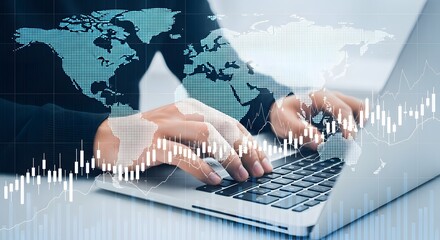 Person typing on laptop with world map overlay and stock market chart in the foreground view