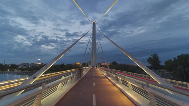 Day to night timelapse of the Alamillo Bridge in Seville, Spain, featuring continuous car traffic and the transformation of daylight into the glowing lights of the city at dusk