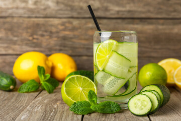 Cucumber water with lemon, lime and mint on a wooden table. Water infused with sliced ​​cucumber in a drinking glass. Tonic refreshing drink. Cucumber lemonade.Summer natural cooling drink.Copy space