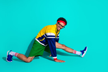 Energetic male athlete in retro outfit stretching with a vivid teal background showcasing a fun and dynamic sporty lifestyle vibe
