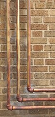 Exposed copper plumbing pipes on a brick wall with a warm industrial texture. Ideal for...