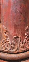 Close-up of an ornate antique cast iron column with rust and red peeling paint, featuring...