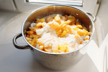 Fresh apricot slices with sugar in a shiny metal pot on a windowsill in daylight, homemade jam...