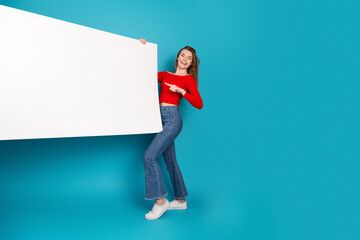 Young woman in casual red top holding a blank white banner on a blue background for advertisements...