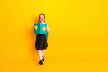 Happy schoolgirl in uniform holding book on yellow background, expressing joy and education