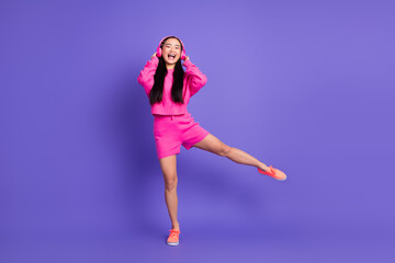 Energetic young woman in bright pink clothing dancing and laughing with a vibrant purple backdrop...