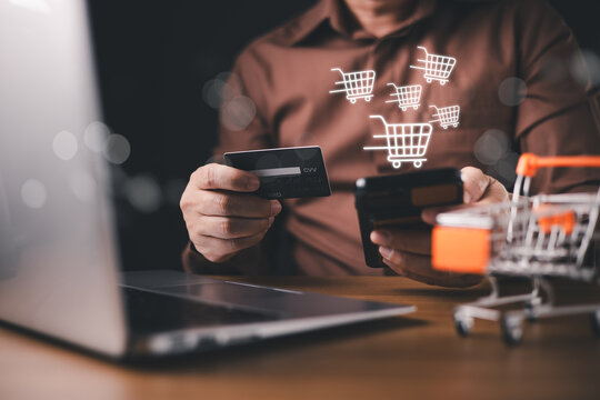 A person holds a credit card and smartphone near a laptop with shopping cart icons, symbolizing online shopping, e-commerce, digital payment, consumer behavior, and mobile retail technology trends.