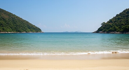 Scenic Beach with Calm Clear Water and Green Hills Under Bright Blue Sky