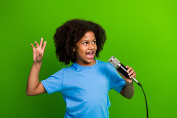 Joyful young girl singing enthusiastically with microphone against vivid green background...