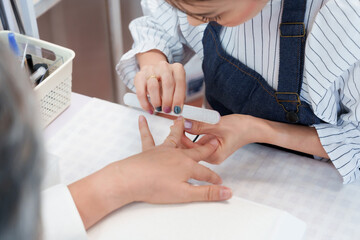 Close-up of nail spa technician filing nails for senior asian woman during professional manicure...
