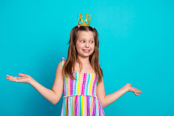 Young girl with crown in colorful outfit smiles on turquoise background raising hands, embracing...