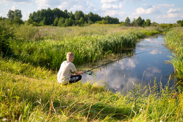 Boy fishing by riverbank on sunny summer day