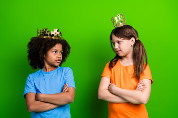 Two schoolgirls wearing crowns, crossing arms, and standing confidently against a green background...
