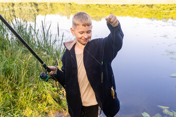 Happy boy showing small fish after fishing success by river