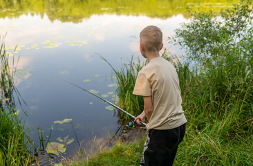 Boy waiting with fishing rod by calm river in green countryside