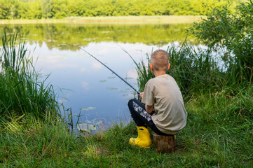 Boy waiting with fishing rod by calm river in green countryside