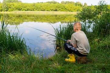 Boy waiting with fishing rod by calm river in green countryside