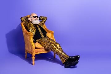 Eccentric older gentleman relaxed on an ornate chair wearing a bold patterned suit and sunglasses against a vibrant purple background