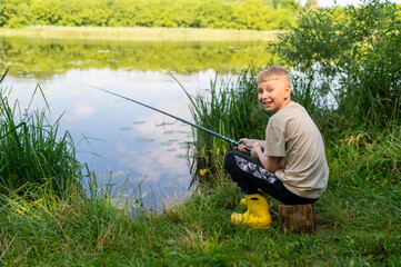 Boy waiting with fishing rod by calm river in green countryside