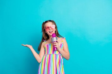 Cheerful young girl in colorful attire singing with a microphone and posing against a vibrant...