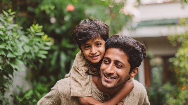 Happy indian father giving piggyback ride to his son and looking at camera. Cute ethnic boy with dad playing outdoor. Close up face of handsome man carrying on shoulders his middle eastern kid., no l