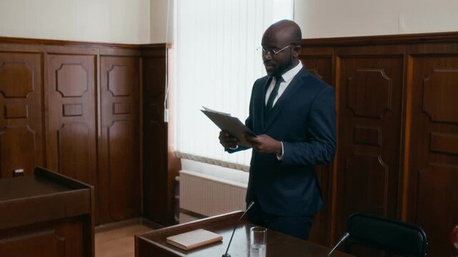 Handheld zoom in shot of African American attorney in formal suit giving speech at lectern in courtroom