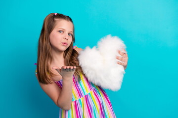 Cheerful young girl holding a white fluffy heart cushion, wearing a colorful summer dress, on a...
