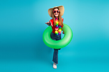 Stylish young woman poses with green inflatable and colorful lei against blue background in...