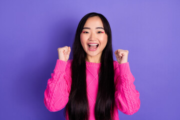 Excited woman in pink sweater expresses joy with clenched fists in vibrant purple background