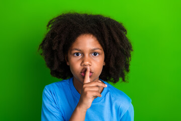 Smiling child with hush gesture against a green background, promoting quietness, calmness, and...