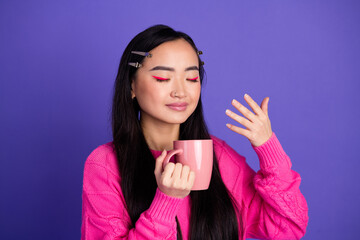 Charming young woman in vibrant fashion enjoys a cup of coffee against a purple background