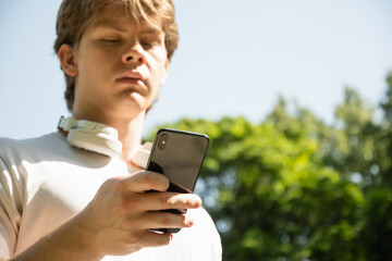 Young caucasian man listen music and holding mobile phone in nature summer background. Check apps,...