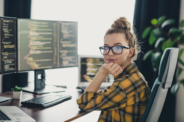 Professional woman programmer working remotely at home, writing code on her computer screens in a...