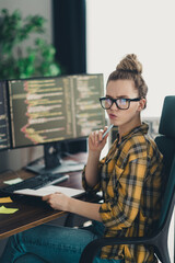 Focused young female programmer analyzing code on computer screen in stylish workspace, working...