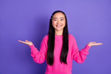Smiling young woman in a pink sweater gesturing joyfully against a vibrant purple backdrop,...