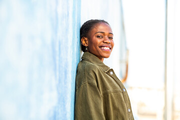 Confident African woman leaning on blue wall with smile