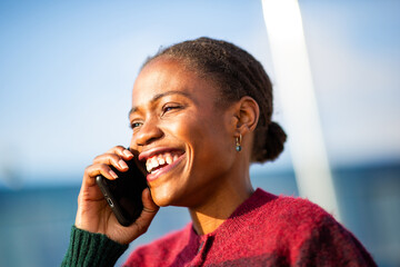 Joyful African woman talking on smartphone under blue sky