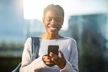 Woman smiling while reading phone message outdoors
