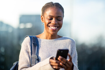 Cheerful woman texting on smartphone with backpack on