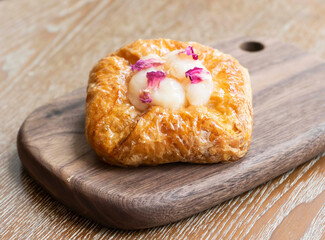 Lychee Rose Danish topped with delicate lychee fruit and fragrant dried rose petals on wooden board side view of Flaky Pastry