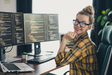 Young female programmer working on coding projects in a modern home office with dual monitors and a...